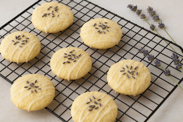 Freshly baked lavender and goat cheese cookies with glaze and lavender buds, cooling on a wire rack with sprigs of lavender beside them